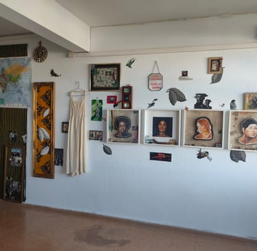 An art gallery wall featuring framed portraits, a world map, a vintage dress, and mixed media artwork.
