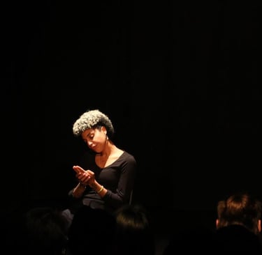 Una mujer afro con un vestido negro sentada en un escenario