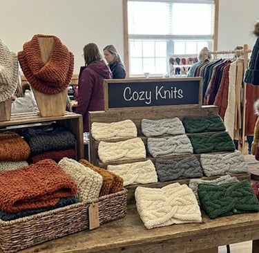 Sales table at a crafting show with knitted cowls and beanie caps