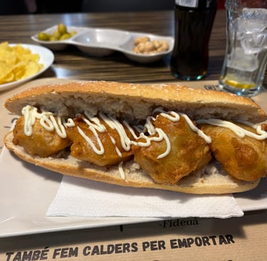 Spanish calamari sandwich with garlic aioli served with potato chips, olives, and a cold drink.