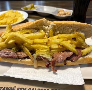 A traditional Spanish steak sandwich topped with crispy golden french fries on a crusty baguette.