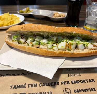 Grilled cuttlefish baguette sandwich with garlic and parsley sauce, served with olives and chips.