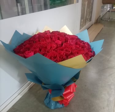 A large bouquet of fresh red roses wrapped in blue and gold paper with a red ribbon.