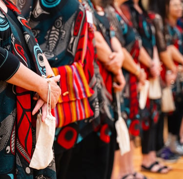 A line of people wearing traditional Indigenous Haida art clothing and carrying small medicine bags.