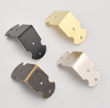 Decorative metal corner protectors in black, brass, silver, and antique bronze finishes for furniture.