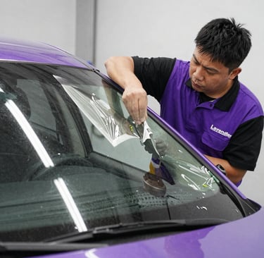 Professional technician applying protective window film to a purple car for tinting and UV protection.