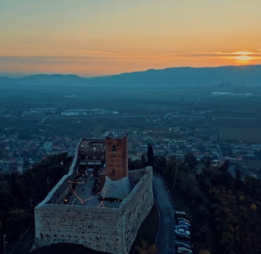Aerial view of a medieval Italian castle at sunset overlooking a scenic valley landscape.
