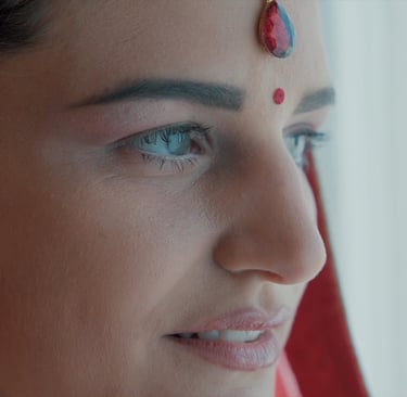 Close-up of a woman wearing traditional Indian bridal makeup with a red bindi and teardrop maang tikka.
