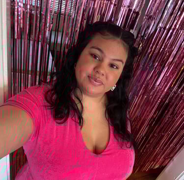 A smiling woman in a pink t-shirt poses in front of a shiny pink foil fringe backdrop.