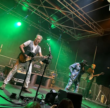 Live rock band performing on an outdoor stage with green lighting and electric guitar player.