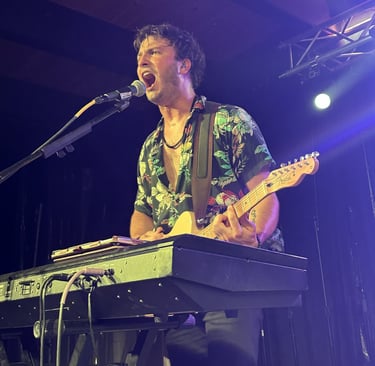 Male musician singing and playing electric guitar and keyboard during a live concert performance.