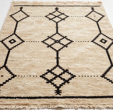 Close-up of a soft, cream-colored Beni Ourain rug with bold charcoal geometric patterns, laid out in a sunlit living room.