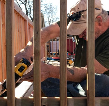 Brewer Construction carpenter installing new deck balusters on an Evergreen property with a power drill.