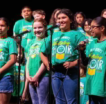 Merced Children's Holiday Choir performing in green t-shirts during a musical concert on stage.