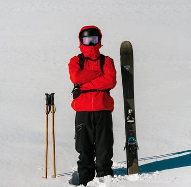 Baptiste Rouge bras croisés avec les batons de ski en bambou a sa droite et ses skis à sa gauche
