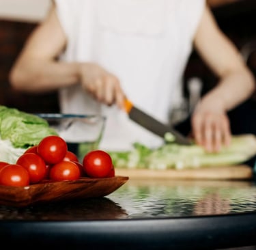 Femme coupant des légumes sur une planche avec des légumes frais au premier plan