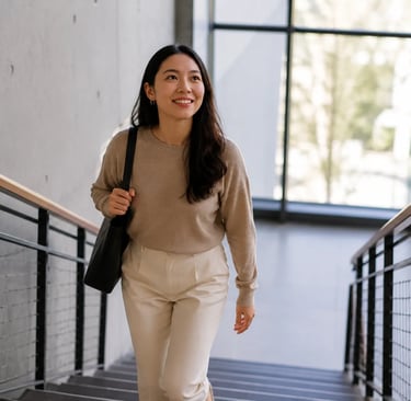 Femme souriante montant un escalier intérieur avec un sac à l’épaule.