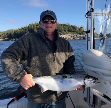A man on a fishing boat holds a large silver salmon caught during a deep-sea fishing trip.