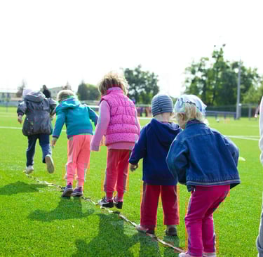 Photo of children standing in a line on a rope laid out on grass in a field