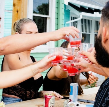 Group of friends cheering with red alcoholic shots at an outdoor patio bar.