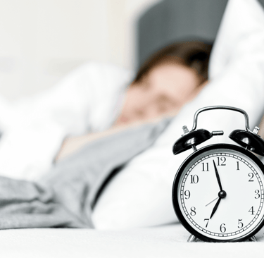 a person laying in bed with a clock on the side of the bed