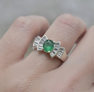 Hand wearing a vintage silver ring with an oval emerald gemstone and tapered baguette diamond accents.