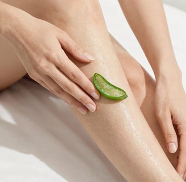A person applying a fresh slice of natural aloe vera leaf to a smooth leg for skin hydration and soothing care.