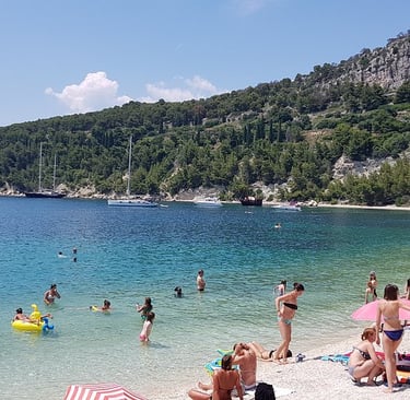 People swimming and relaxing at Kašjuni Beach in Split with crystal clear sea and pine-covered hills in the background