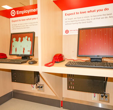 Two retail employment kiosks with computers, red telephones, and professionally managed network equipment installed below.