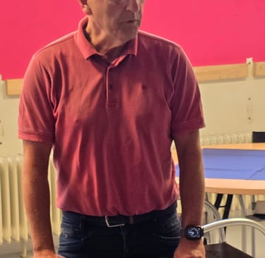 Senior man in a pink polo shirt and glasses standing in a room with a bright pink wall.