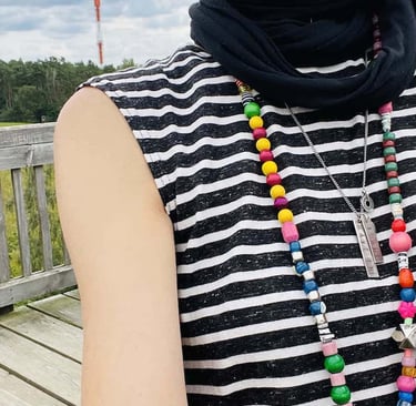 samuko wearing a striped sleeveless shirt and colorful beaded necklaces on a wooden boardwalk.