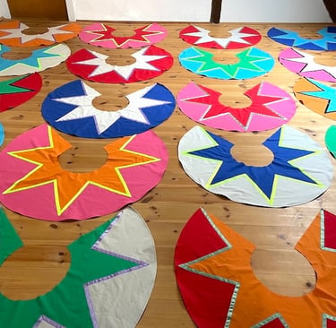 Handmade colorful circus costumes with star patterns laid out on a wooden floor.