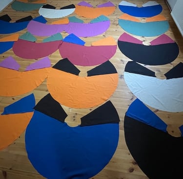 Handmade colorful circle capes in various vibrant fabrics laid out on a wooden floor for sewing.