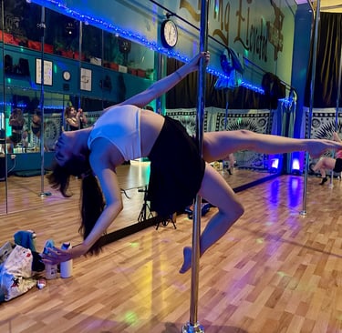 Side view of Ryanne hitting a leaned back pose on a pole at a dance studio.