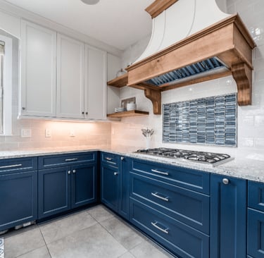 Modern kitchen featuring navy blue cabinets, white granite countertops, and a rustic wood range hood.