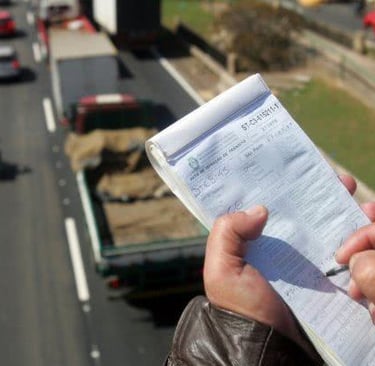 Traffic officer writing a speeding ticket above a busy highway with trucks and cars.