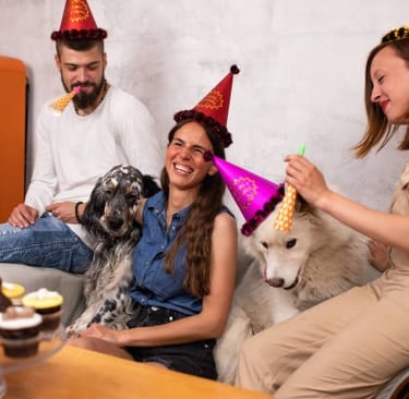 Amigos con sombreros de fiesta celebran un cumpleaños con sus perros y pastelitos.