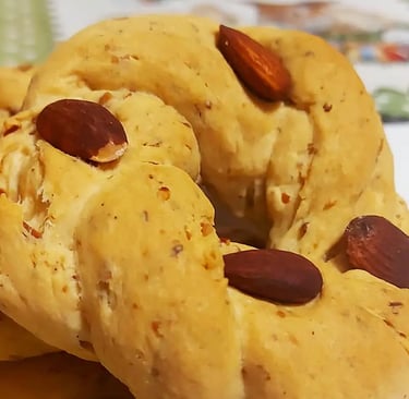 Traditional Italian taralli dolci biscuits topped with whole almonds on a white plate.