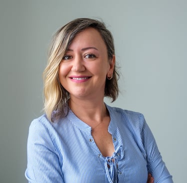 Professional portrait of a smiling woman with blonde highlights wearing a blue striped shirt.