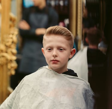 Niño pequeño con corte pompadour estilizado usando capa en una barbería profesional.