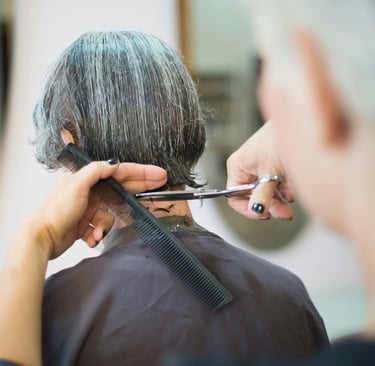 Estilista profesional cortando el cabello corto de un cliente con peine y tijeras en un salón.