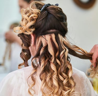 Estilista profesional aplicando extensiones rubias rizadas a una clienta para un peinado de boda.v