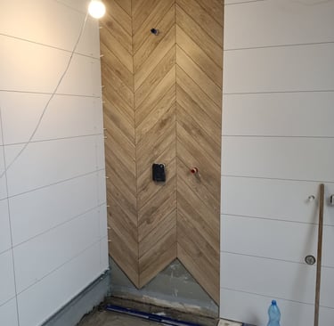 Modern bathroom shower renovation featuring vertical oak herringbone tiles and white wall panels.