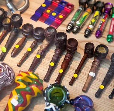 A variety of wooden, glass, and metal smoking pipes displayed on a wooden surface in a head shop.