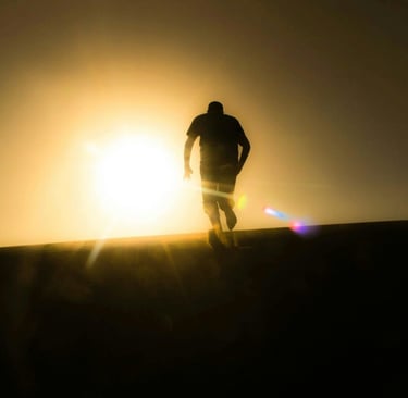 a man walking on a hill with a sun shining through the sun