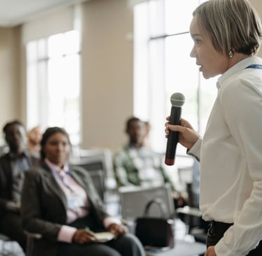 Professional female speaker holding a microphone and addressing a diverse audience at a business conference.