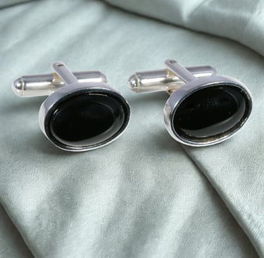 Elegant oval black onyx cufflinks set in sterling silver on a luxury silk fabric background.