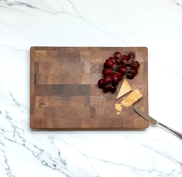 Overhead view of a wooden chopping board styled with grapes, cheese and a knife