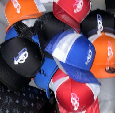 A pile of assorted colorful trucker hats and snapback caps with embroidered logos in blue, red, and orange.