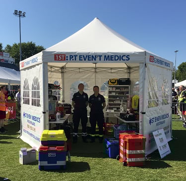 Event medical staff stand inside a white first aid tent equipped with emergency supplies at an outdoor festival.